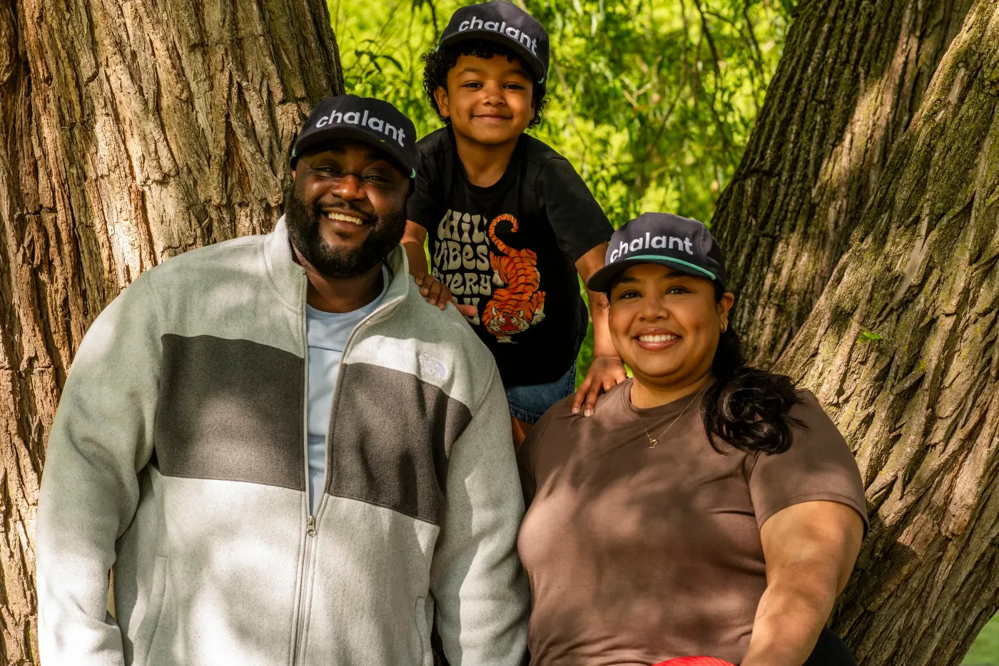 A family wearing Chalant hats, smiling together against a tree