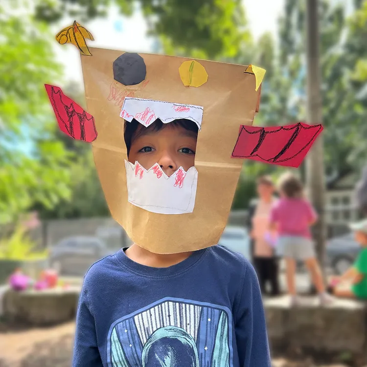 A child in a handmade paper-bag mask at Camp Gedi